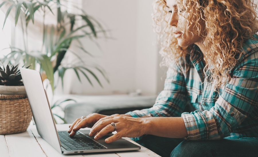 A person sitting on a couch typing on a laptop situated on the coffee table in front of them