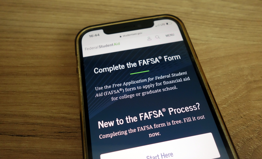Cell phone on wooden table displaying FAFSA homepage