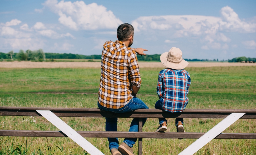 Man and boy sitting on fence at a farm