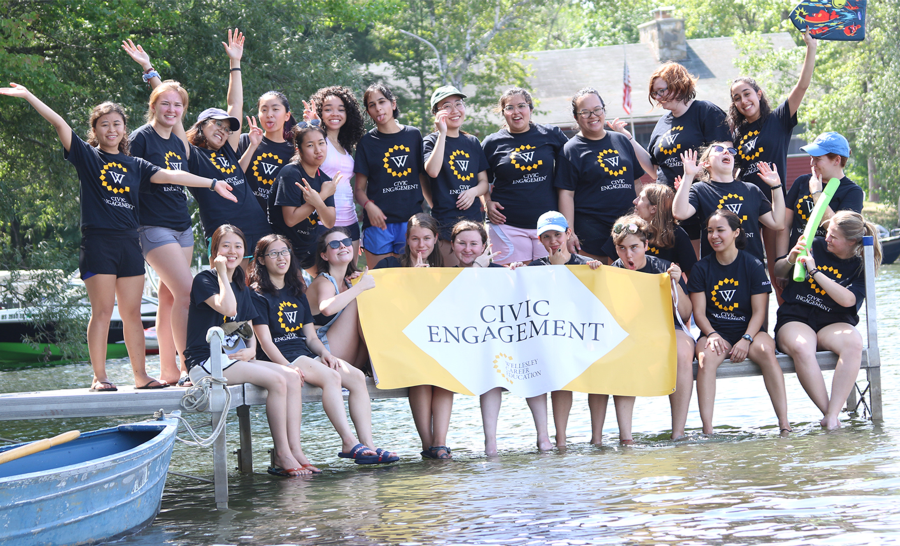 Wellesley College Students Sitting Outside on Pier Holding Banner that Says 