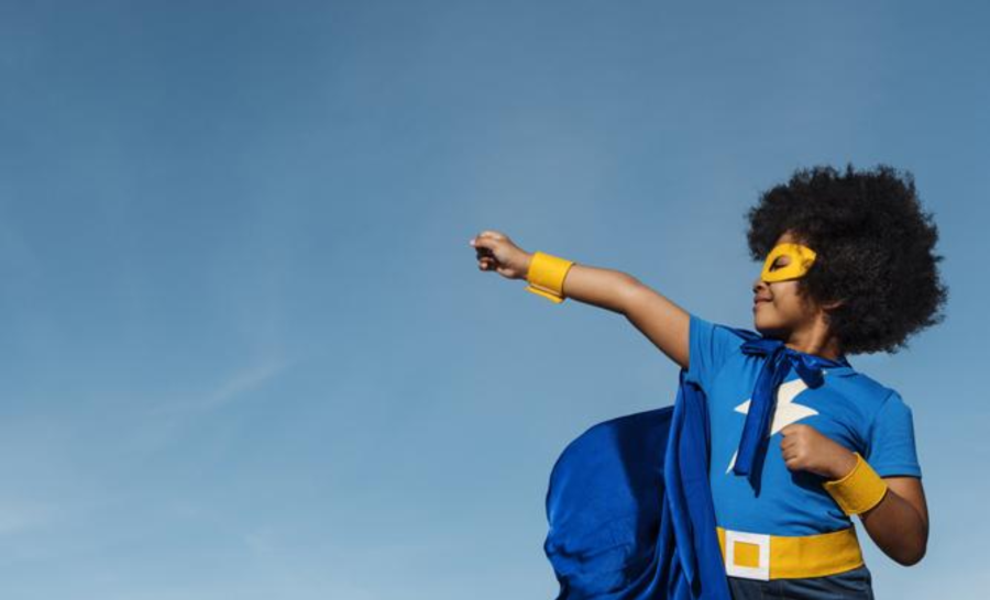 Child dressed like superhero in front of blue sky