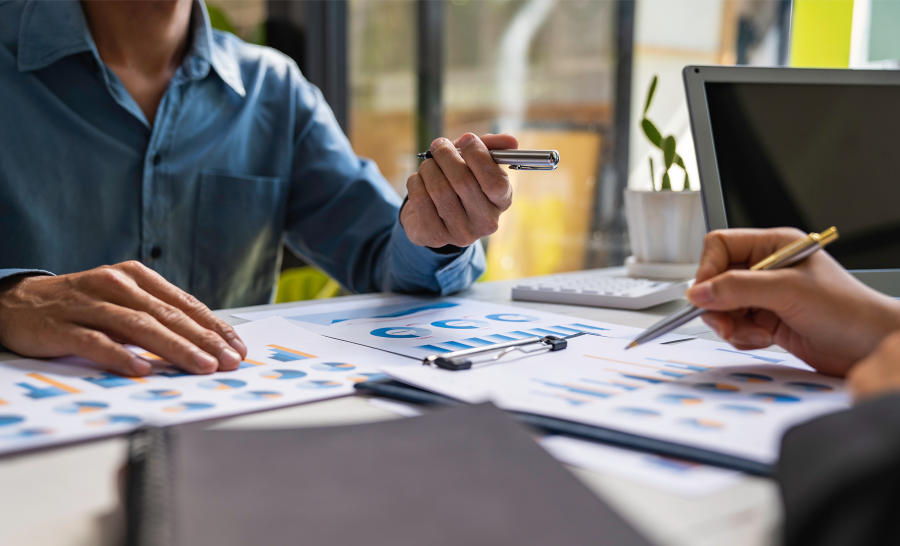 Table covered in papers featuring charts and graphs with two people's hands pointing at specific figures