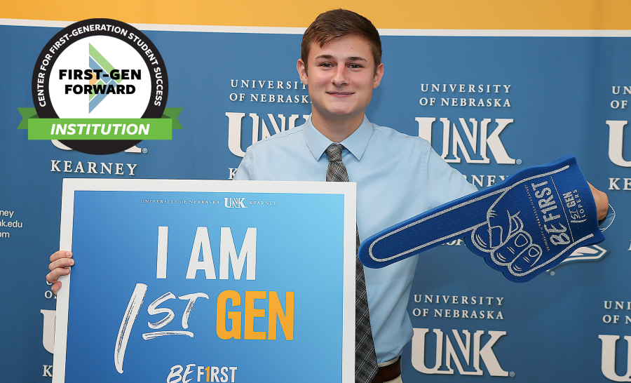 UNK Student Posing in Front of Step and Repeat with Foam Finger and Holding I'm First Sign
