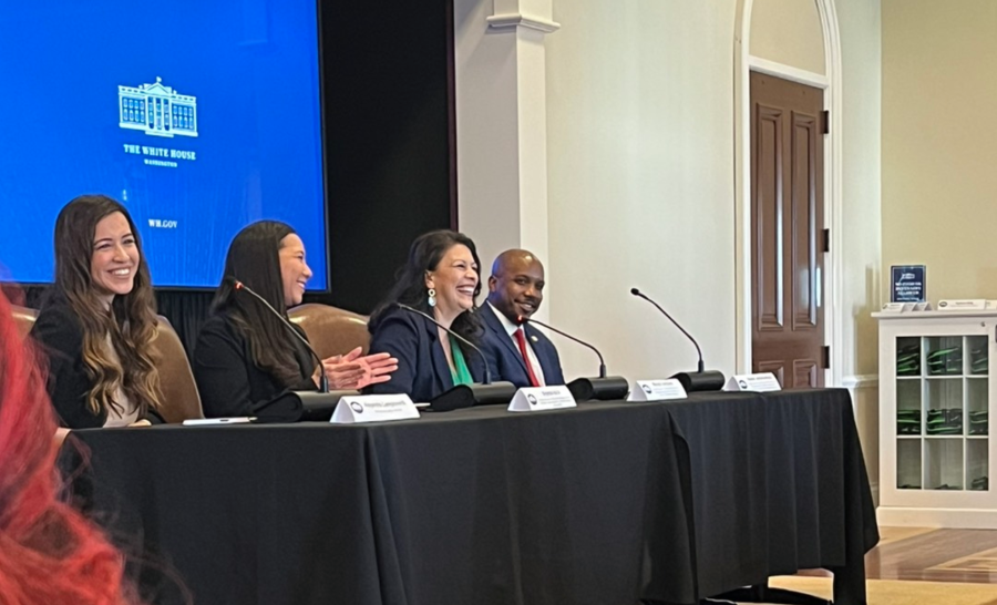 Four panelists seated at table before a blue slide with White House logo
